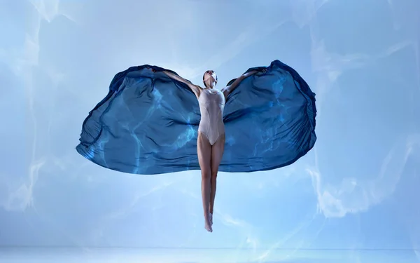 青い背景の上に絹の生地で優雅な動きで飛んで若いバレリーナ アート モーション アクション 柔軟性 インスピレーションのコンセプト コンテンポラリーダンスの美しさ — ストック写真
