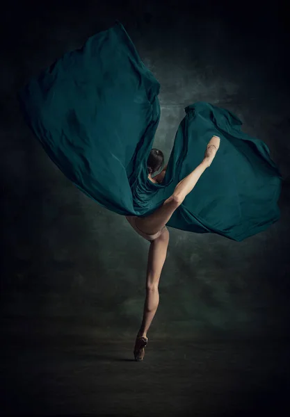 On tiptoe. Portrait of beautiful ballerina wearing beige bodysuit dancing with fabric over dark background. Concept of classic ballet, inspiration, beauty, dance, creativity