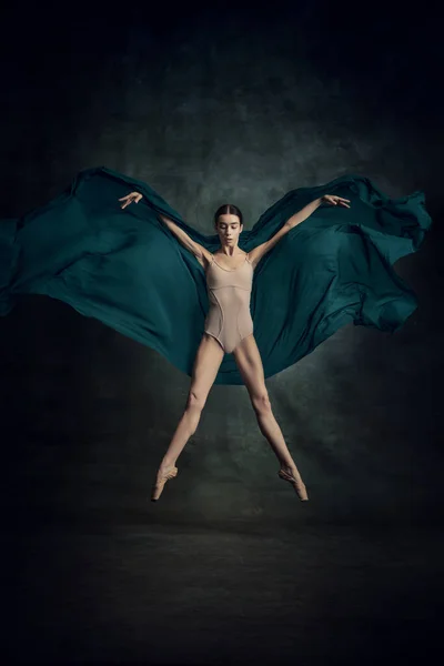 Graceful jump. Portrait of beautiful dancer flying with silk fabric over dark green background. Contemporary dance. Concept of classic ballet, inspiration, beauty, dance, creativity