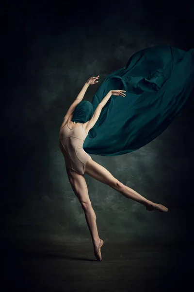 Solo performance. Shot of one adorable ballerina dancing with elegance hands and silk fabric over dark green background. The art, artist, movement, action and motion concept. Beauty of ballet