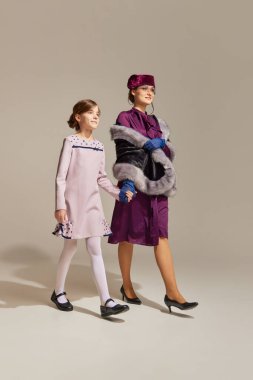 Eğlenceli bir yürüyüş. Çekici anne ve küçük kızın portresi. El ele yürüyorlar ve arka planda gülümsüyorlar. Eski tarz, moda, tatil kavramı, 60 'lar, 70' ler, seyahat