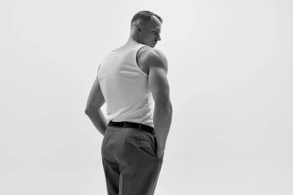 Aesthetics of male body. Portrait of muscular male fashion model wearing white t-shirt and posing over studio background. Concept of fashion, style, mens health, beauty, body care, fitness. Back view