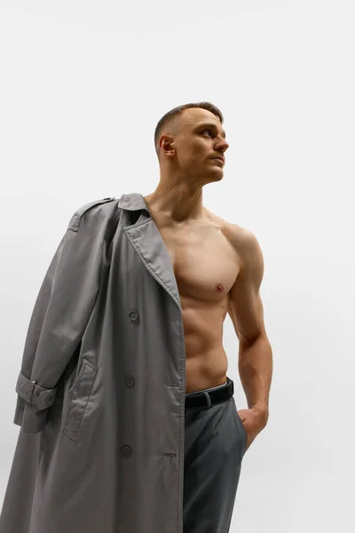 拍的英俊男子与运动体形持有外套的肩膀 并展望了白色工作室的背景 男性时尚 身体美学 美容美发 男性健康 情感的概念 — 图库照片