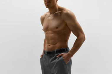 Atletik vücut, vücut. Beyaz stüdyo arka planında üstsüz poz veren kaslı genç adamın yüzsüz fotoğrafı. Erkek modası, stil, vücut estetiği, güzellik, erkek sağlığı, spor, reklam