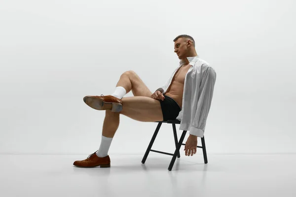 一个有魅力的男人坐在椅子上 穿着没有扣子的衬衫 从白色的工作室背景眺望远方 男子气概和力量 男性健康 男性身体美丽的概念 — 图库照片