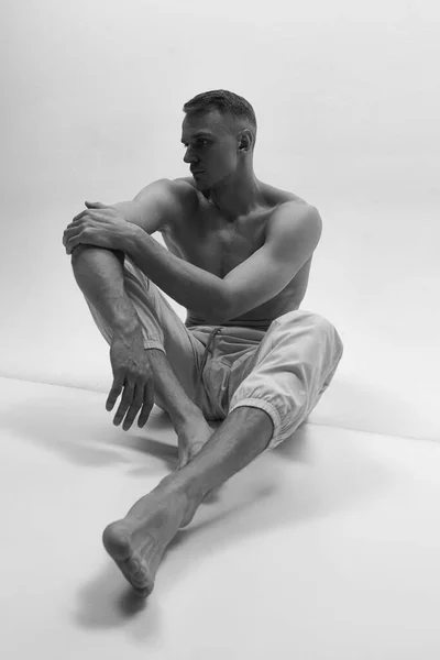 在工作室背景的地板上坐着一个英俊的无上衣 体形活泼的男人 黑人和白人 男性时尚 身体美学 广告的概念 — 图库照片