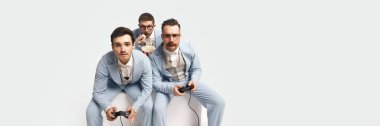 Oyunlar. Playstation 'da oynayan takım elbiseli üç arkadaşın portresi. Beyazların arka planında ciddi bir suratı var. Fotokopi alanı olan pankart. Dönem, retro, vintage, duygu karşılaştırması kavramı