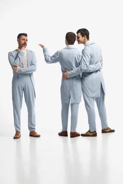 Conversation. Shot of three men, friends wearing old style clothes and discuss business emotionally over white studio background. Concept of comparison of eras, retro, vintage, emotions, friendship