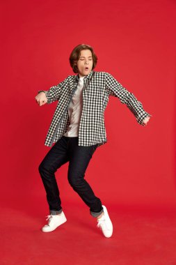 Sınavı geçtim. Genç bir çocuk, günlük kıyafet giyen bir öğrenci kırmızı stüdyo arka planında zevkle dans ediyor. Eğitim kavramı, insani duygular, ruh hali, psikolojik durum, güzellik, reklam