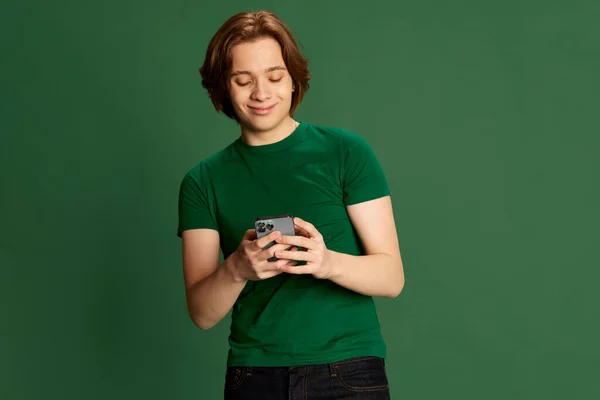 友達とおしゃべり 若い学生のポルタリオ 長い髪を手に携帯電話を保持し 緑のスタジオの背景に喜びと笑顔男 人間の感情 社会的ネットワークの概念 — ストック写真