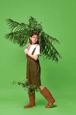 Yağmur mevsimi. Yeşil arka planda şemsiye yerine avuç içi ile ayakta duran çizme giyen çekici bir genç kız. Güzellik kavramı, insani duygular, ruh hali, sanat, modern moda, reklam