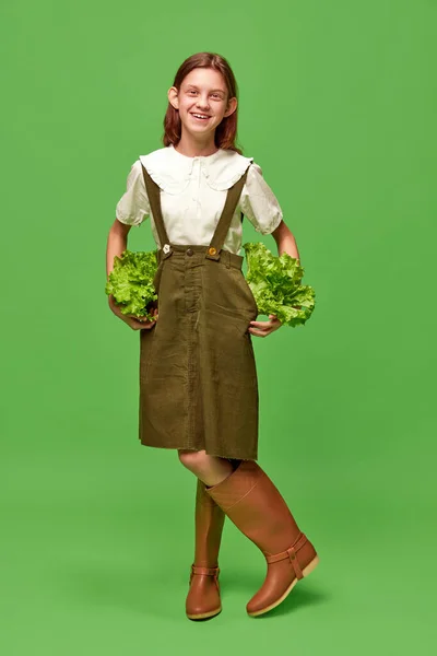 健康的な食事 ガーデニング服を着てサラダを持った笑顔の可愛い女の子の肖像画 緑の背景に収穫 美しさの概念 人間の感情 アート 現代的なファッション — ストック写真