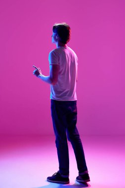 Genç bir adam, beyaz t-shirt giyen ve pembe arka planı işaret eden neon ışıklı bir adam. Arkadan bak. Oyun kavramı, dijitalleştirme ve teknoloji, iç dünya