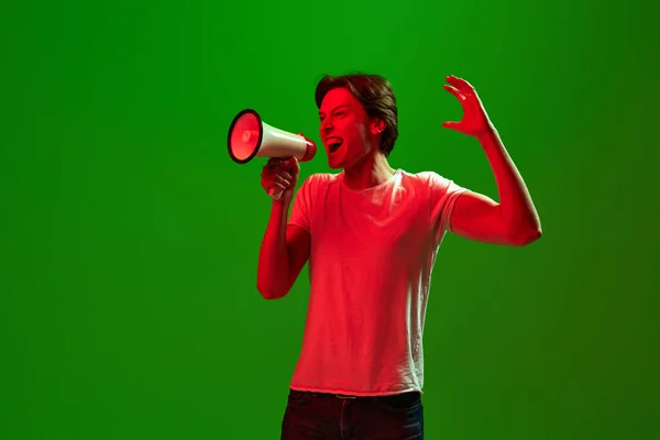 気をつけて ある若い怒っている男 ネオンで緑の背景にメガホンを通して叫んでいる男 ソーシャルメディア 人間の感情 広告の概念 — ストック写真