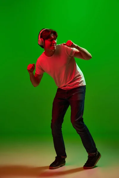 ダンス 好きなメロディー 刺激的な若い男 ヘッドフォンを着て音楽を聞いて 緑のネオンの背景に手で踊る男 人間の感情 広告の概念 — ストック写真