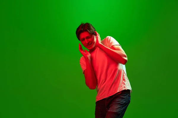 懐疑的な男だ 若い男の肖像画 男はネオンの光の中で緑の背景に不確定な顔の表情で立ってシャツを着て 若者の概念 人間の感情 — ストック写真