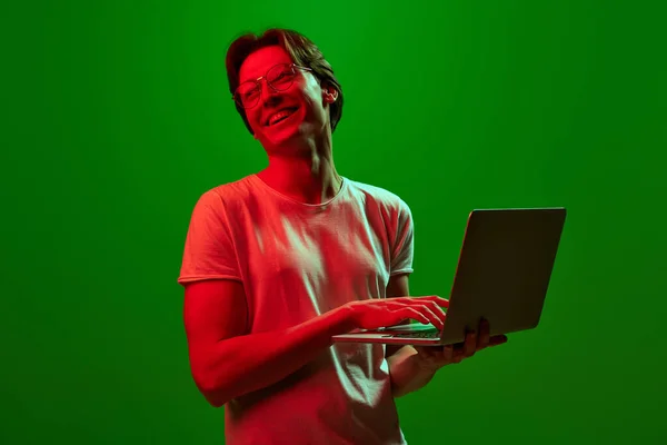 远程工作 自由职业者 微笑的小伙子 拿着笔记本电脑的推销员 带着绿色霓虹灯背景的快乐工作 人类情感 广告的概念 — 图库照片