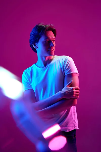 Personal space. One young guy, man with calm face standing and looking away over pink background in neon light. Solitude. Concept of youth, human emotions, facial expression, ad