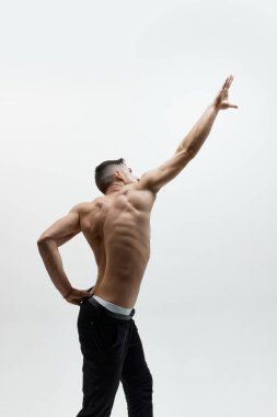Siyah kot giyen, beyaz arka planda üstsüz poz veren çekici bir adamın stüdyo fotoğrafı. Kaslı vücut şekli. Erkeklerin moda, tarz, vücut estetiği, güzellik, erkek sağlığı, duygu kavramı