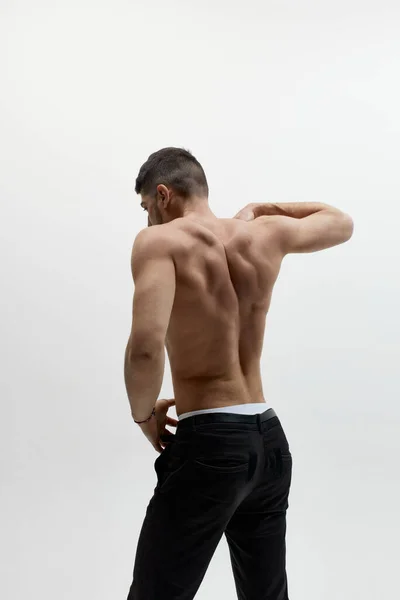 Portrait of attractive muscular man with wide back posing over white studio background. Back view. Masculinity and confidence. Concept of mens health, beauty, fashion, ad