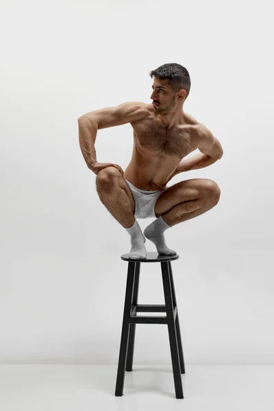 一个体形匀称的男人站在椅子上 有着严肃的面部表情 有着白色的工作室背景 身体美学 男人健康的概念 — 图库照片
