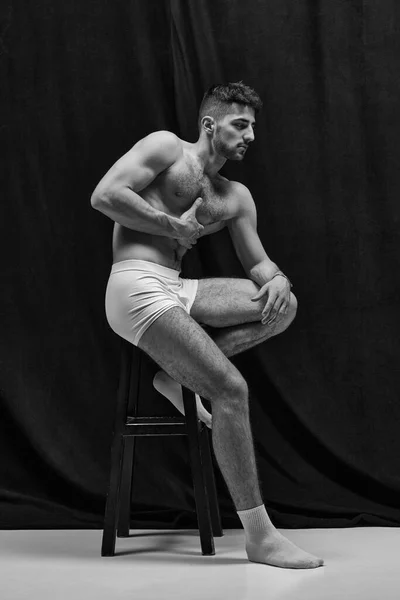 Aesthetics of male body. Portrait of handsome young muscular man in underwear posing shirtless over white studio background. Masculinity and strength. Concept of mens health, beauty of male body