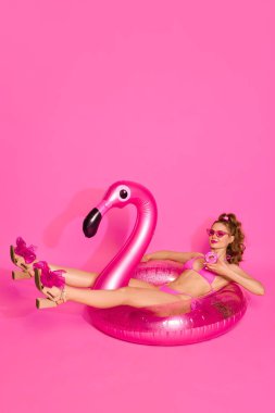 Yaz Cheeling 'i. Mayo giymiş, elinde donut tutan sarışın bir kızın portresi ve pembe stüdyo arka planında şişme flamingoya uzanmış. Yaz kavramı, tatil, parti, moda, güzellik, gençlik, reklam