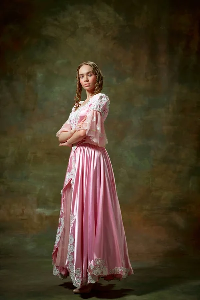 Serious lady. Portrait of charming blond girl, princess wearing fancy pink dress and standing with folded hands over vintage texture background.Concept of medieval, beauty, old-fashioned clothes, ad