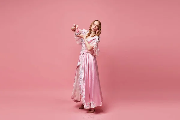神々の食べ物 甘い歯 ピンクのスタジオの背景に喜びと綿のキャンディーを食べるルネサンスのドレスを身に着けている空腹のおとぎ話ブロンドの王女 中世の概念 美しさ バロック — ストック写真