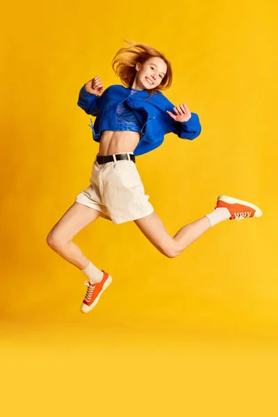 Feel of freedom. Studio shot with young, gorgeous red haired girl jumping and smiling over yellow studio background. Concept of human emotions, youth, happiness, mood, leisure time, ad
