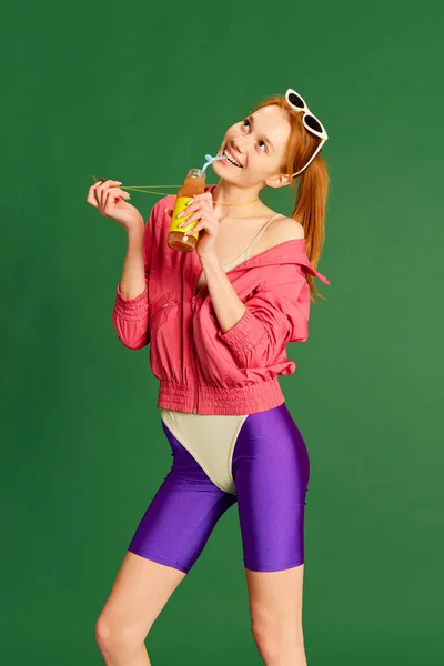 バランスの取れた食事 ビタミン 緑のスタジオを背景に楽しそうにジュースを飲むスポーツ服を着た若い美少女の肖像画 健康食品 スポーツ 広告コンセプト — ストック写真