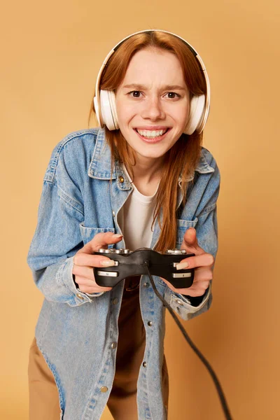ゲーム中毒だ 若い濃縮された女の子の肖像画 10代の若者はヘッドフォンを着用し 生姜の背景にビデオゲームで遊ぶ オンライン デジタル ライフスタイル 感情の概念 — ストック写真