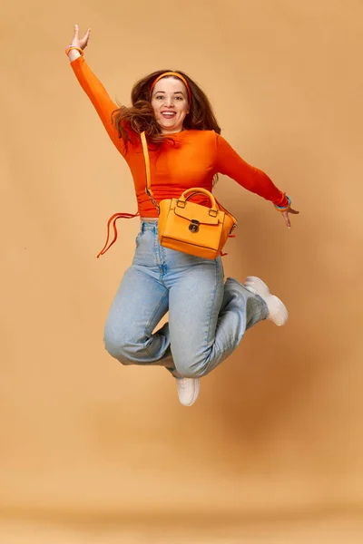 空中浮遊 きれいな女の子の肖像画 学生の明るい服を着て ジーンズジャンプし 生姜スタジオの背景に笑みを浮かべて ファッション 美しさ ライフスタイル 人間の感情 広告の概念 — ストック写真
