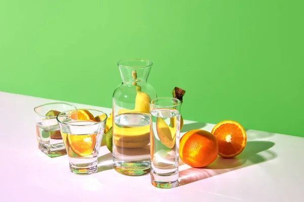 stock image Fruit detox. Still life with fresh fruits kiwi, banana, orange and glasses with water on table over green background. Bright colors. Concept of healthy food, diet, nutrition, weight loss, vitamins