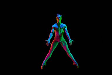 Renkli bir vücut. Çekici genç bir erkek, balerin zıplayan yıldız. Karanlık stüdyo arka planında, neon ışığıyla havada poz veriyor. Uzayı metin için kopyala. Zarafet, sanat, güzellik, çağdaş dans konsepti