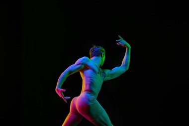 Güç, özgürlük. Genç, esnek atletik bir adam, yakışıklı bir dansçı, elleri yukarıda, karanlık stüdyo arka planında, neon ışığı altında poz veriyor. Modern bale tarzı. Grace, sanat, profesyonel spor konsepti.