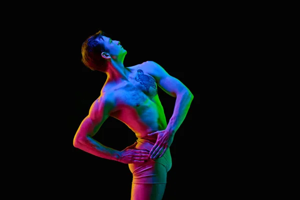 stock image Dreaming dancer. Portrait of one young attractive man, actor with naked torm posing over dark studio background with neon light. Weightless, flexible. Grace, art, beauty, contemporary dance concept