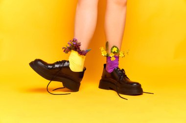 Bahar havası. Sarı stüdyo arka planında klasik ayakkabılar ve kır çiçekleri giyen komik kadın portresi. Moda kavramı, şık kıyafetler, yemek, güzellik, sanat, yaratıcılık