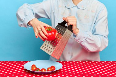 Yemek zamanı. Süslü gömlek giyen bir kadın portresi mavi arka planda, festival masasının yanında domatesli yemek hazırlıyor. Organik tarım yiyeceği. Sağlıklı yaşam tarzı, diyet, vitamin, fitness, reklam kavramı