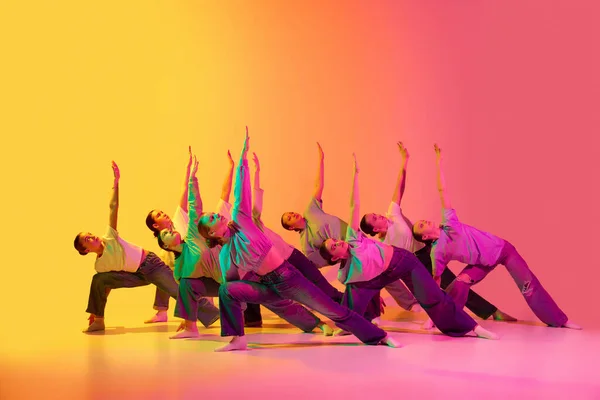同期性 ネオンの光の中でピンクと黄色のグラデーションの背景で一緒に踊る白いTシャツとジーンズを身に着けている美しい十代の女の子のグループ モダン フリースタイル ダンス 現代美術のコンセプト — ストック写真