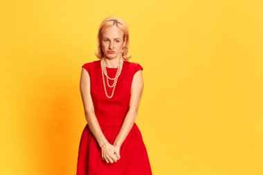 Utangaçlık, belirsizlik. Sarı arka planda suçlu bir yüzle aşağı bakan eski moda elbiseli güzel sarışın kadın portresi. Duyguların kavramı, moda, güzellik, bağbozumu, retro, ad