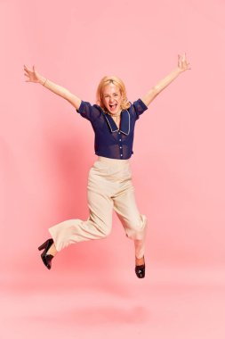 Kutlama, parti. Gülümseyen sarışın bir kadının portresi sevinçten havalara uçuyor ve elleri açık atlıyor pembe stüdyo arka planında. Duyguların kavramı, iş, kariyer, moda, güzellik, vintage, ad