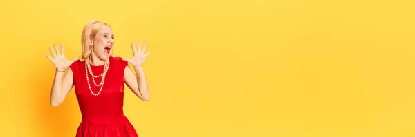 Scare someone. Portrait of blond woman wearing red dress and screaming with hands over yellow background. Banner with copy space. Concept of human emotions, fashion, beauty, vintage, retro, ad