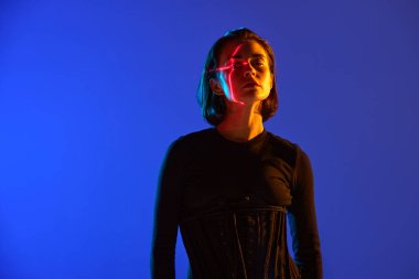 Siyah elbiseli çekici bir kadının portresi ve yüzünde kırmızı bir çizgi ve mavi mod neon arka planından kameraya bakıyor. Dijital sanat kavramı, online, moda, siber punk, fütürizm