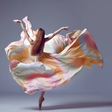 Tek kişilik performans. Gökkuşağı elbisesi giyen balerin gri stüdyo arka planında zarif bir şekilde dans ediyor. Çağdaş dansın güzelliği. Sanat, hareket, eylem, esneklik, ilham kavramı