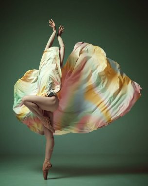Parmak ucunda duruyorum. Gökkuşağı elbisesi giyen zarif bir balerin koyu yeşil stüdyo arka planında zarif dans ediyor. Çağdaş dansın güzelliği. Sanat, hareket, esneklik, ilham kavramı