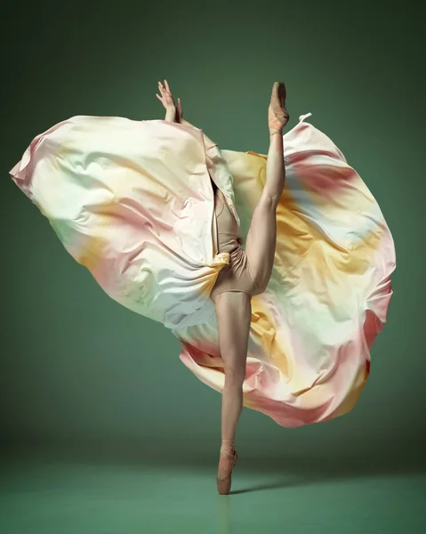 身体の柔軟性を示す 濃い緑の背景にカラフルなドレスを身に着けている1人の若い愛らしいプロのバレエダンサー 古典バレエ 現代美術 ダンスの概念 — ストック写真