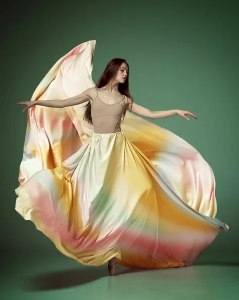 彩虹裙年轻的芭蕾舞演员舞姿优雅 优雅的舞姿与飘扬的面料笼罩在深绿色的工作室背景之上 当代舞蹈的美丽 灵活性 广告概念 — 图库照片