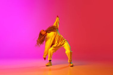 Genç stil sahibi bir kızın portresi, gündelik kıyafetler içinde hip-hop dansçısı eğitimi neon ışıklarıyla değişen pembe arka plan. Gençlik kültürü, hareket, sokak tarzı, moda, aksiyon, çağdaş dans tarzı