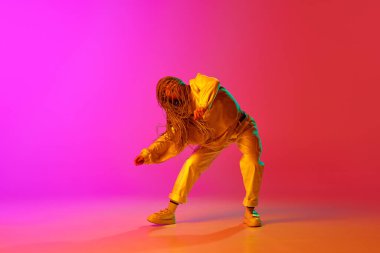 Genç, profesyonel bir hip-hop dansçısı şık kıyafetler giyiyor ve neon ışıkta ilham verici pembe arka planda hareket ediyor. Çağdaş dans stili kavramı, hareket, moda, hobi, sanat, reklam